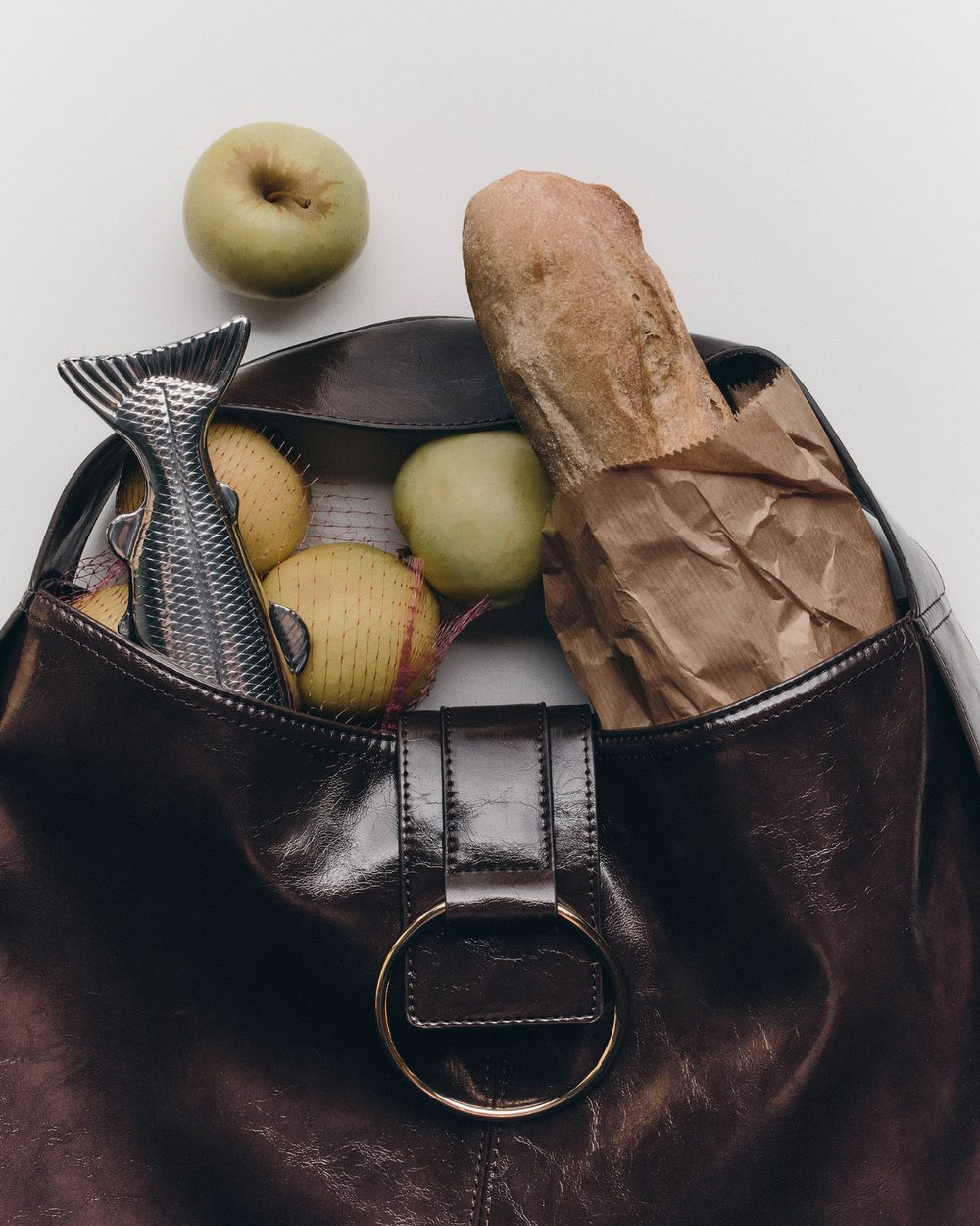 Leather bag filled with a baguette, apples and a fish